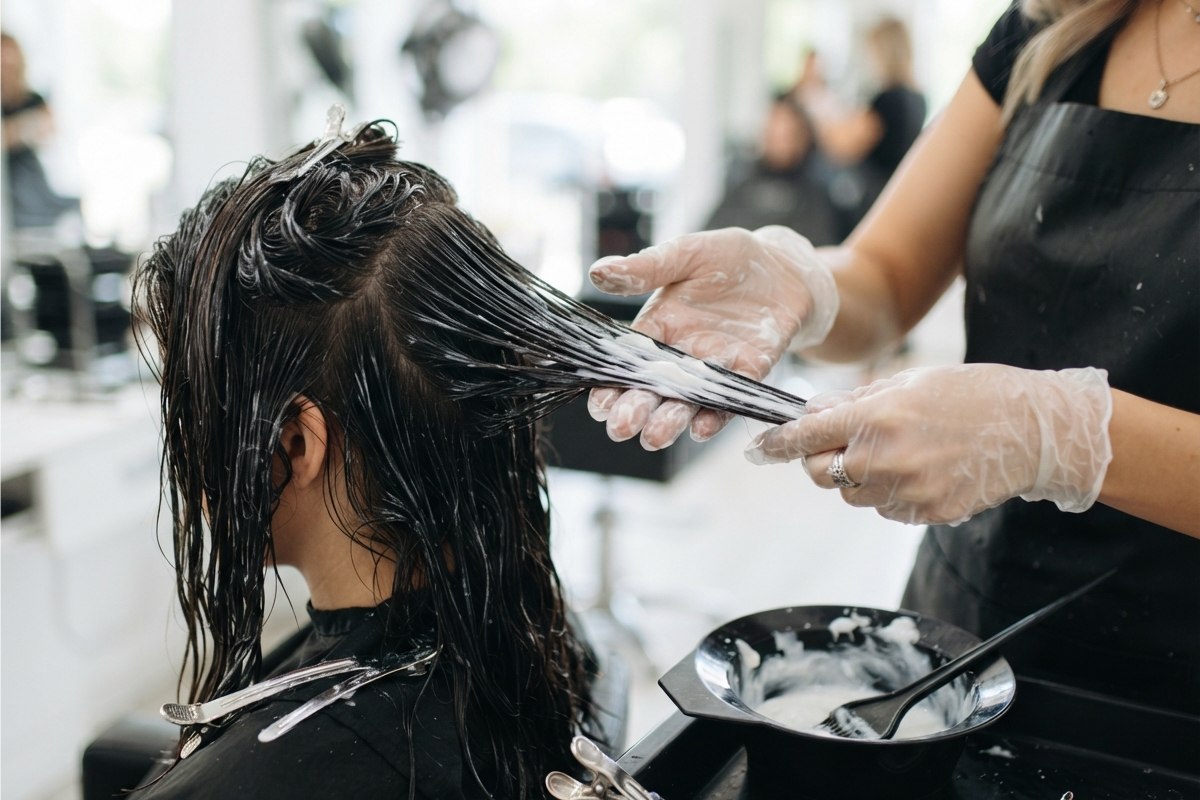 Mãos aplicando creme de queratina em mechas de cabelo molhado
