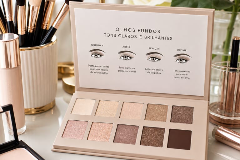 Paleta de sombras com tons claros e brilhantes em uma mesa de maquiagem organizada, com pincéis e outros produtos de beleza ao redor.