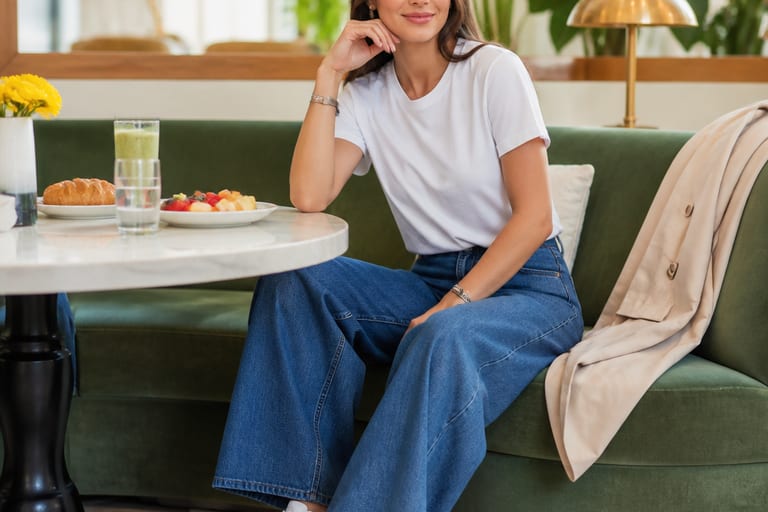 Mulher usando calça jeans wide leg, camiseta básica e tênis brancos em um brunch, em um ambiente iluminado e alegre.
