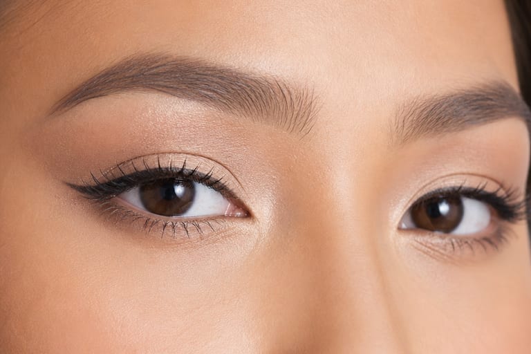 Close em olhos maquiados com sombras claras e delineador, em ambiente iluminado, destacando a técnica de maquiagem para olhos pequenos.