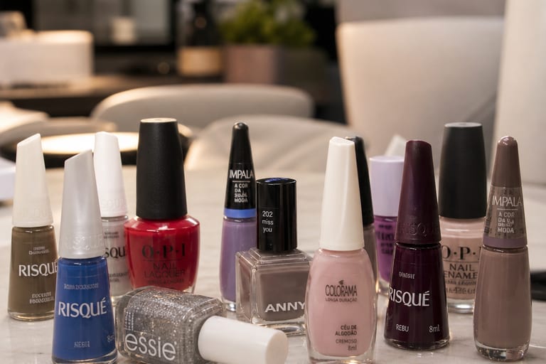 Vários esmaltes em diferentes cores e texturas dispostos em uma mesa de manicure, com foco em marcas conhecidas.