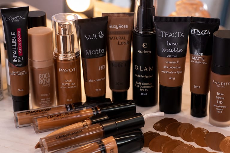 Produtos de maquiagem em tons variados, focando em bases e corretivos, dispostos em uma mesa bem iluminada, destacando opções para peles negras.