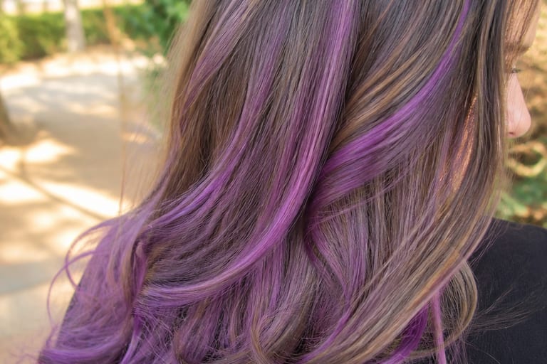 Close em cabelo mega hair com mechas coloridas em ambiente externo, destacando brilho e textura dos fios.