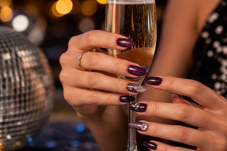 Mãos com unhas de gel decoradas para festa, em ambiente festivo e iluminado, com cores vibrantes e detalhes em glitter.