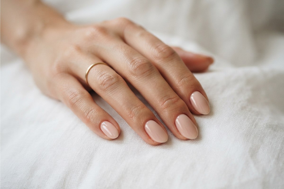 Mão feminina com unhas curtas amendoadas em esmalte nude rosado sobre tecido branco